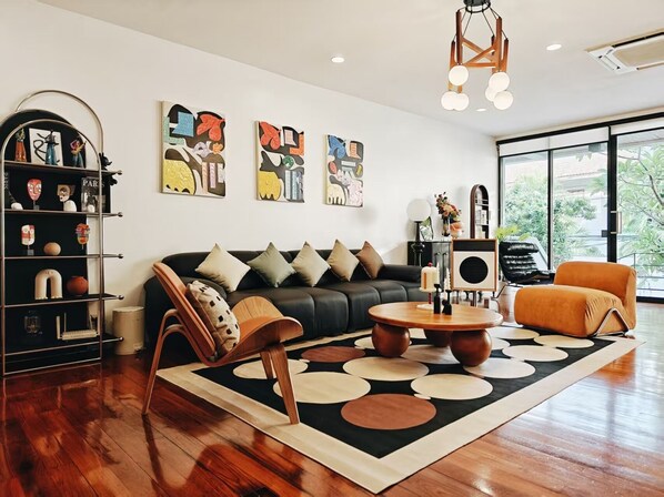 Un salon moderne avec un canapé en cuir noir, des fauteuils en bois, une table basse et des œuvres d’art abstraites accrochées au mur.