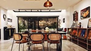 A dining area with a large table, four chairs, a chandelier, and a view through a large window.