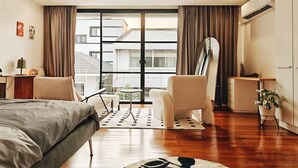 A modern hotel room with a bed, two chairs, a desk, and a large window with curtains.