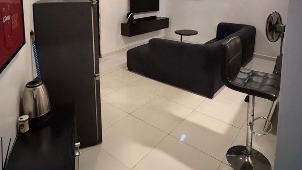A modern living room with a black sofa, a TV, a coffee machine, and a small round table. - Cozy & Convenient 1-Bedroom in Vibrant Victoria Island, Lagos (Lagos)