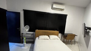 A bedroom with a bed, a desk, a chair, an air conditioner, and a fan. - Cozy & Convenient 1-Bedroom in Vibrant Victoria Island, Lagos (Lagos)