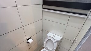 A small, tiled bathroom with a toilet, a hand dryer, and a trash bin. - Cozy & Convenient 1-Bedroom in Vibrant Victoria Island, Lagos (Lagos)
