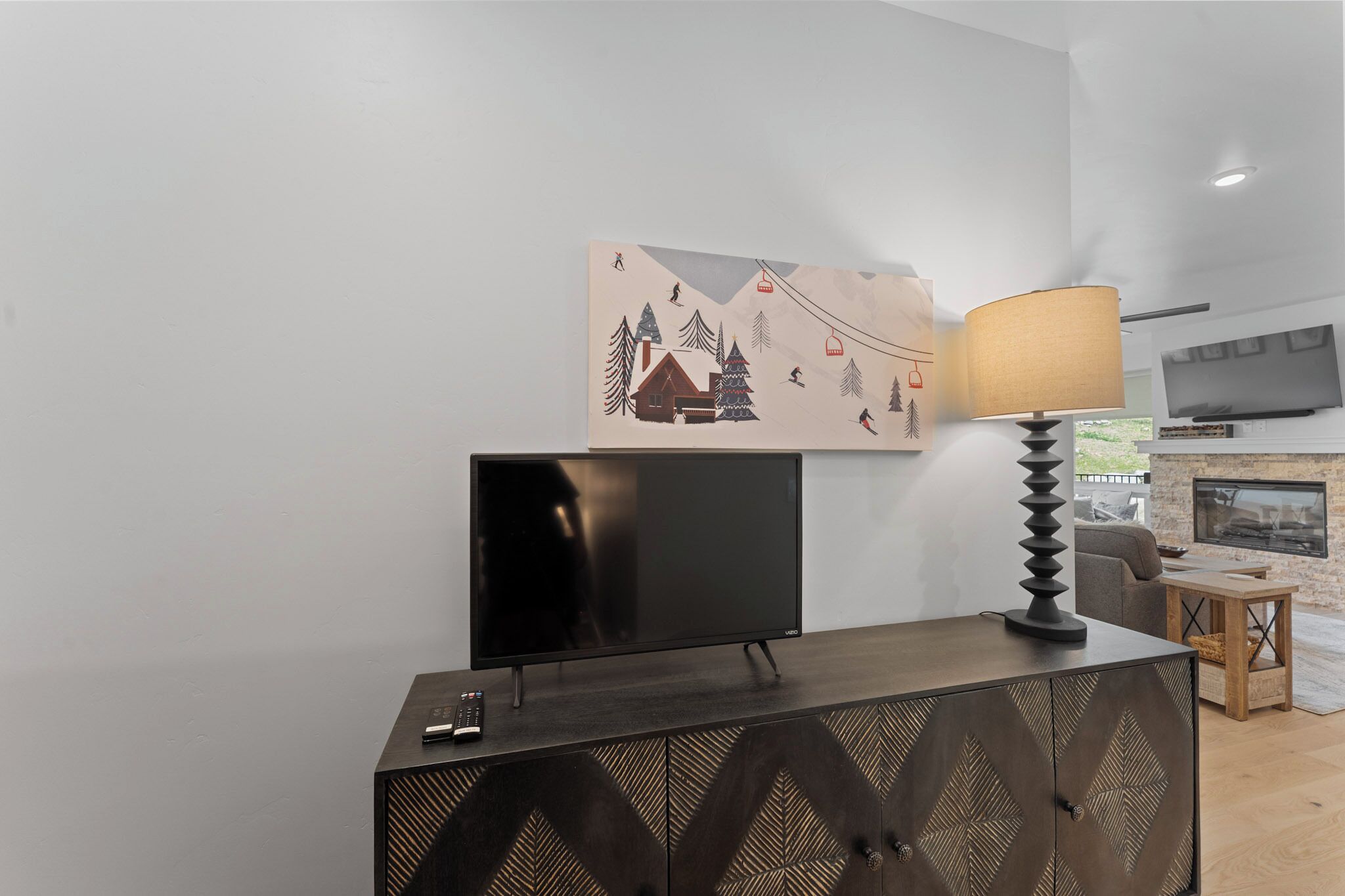 A modern living room with a flat-screen TV on a dark wooden cabinet, a wall-mounted painting of a snowy landscape, a floor lamp, a sofa, and a fireplace.