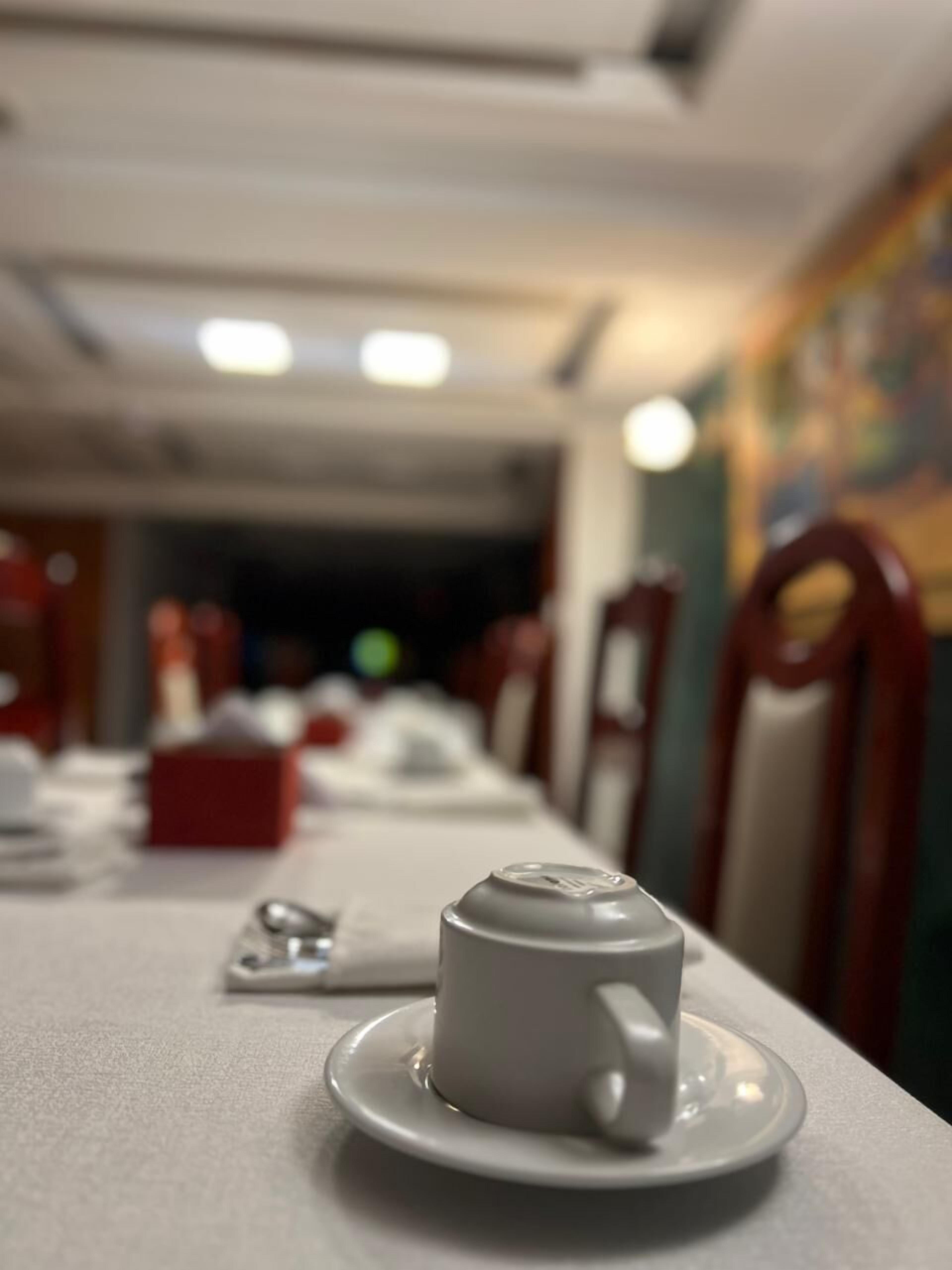 A dining table with a white cup and saucer in the foreground, a red box, and a spoon on the table.