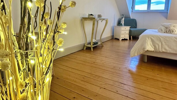 Un dormitorio con piso de madera, una cama, una mesita de noche y una lámpara colgante. Se ve una ventana con vistas.