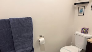 Une salle de bain comprenant des toilettes, un rouleau de papier toilette, une poubelle bleue et un porte-serviettes avec deux serviettes.
