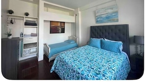 Une chambre à coucher avec un lit, un ventilateur de plafond, une table de chevet, une commode et un tableau au mur.