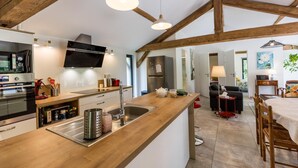 A modern kitchen with wooden beams, a built-in oven, a sink, and a dining area with a table and chairs. - Gîte du Caché - LABRIT - Gîte (LABRIT)