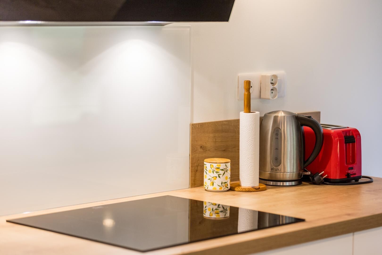 Een keukenblad met een broodrooster, een waterkoker, een rol keukenpapier en een kleine container.