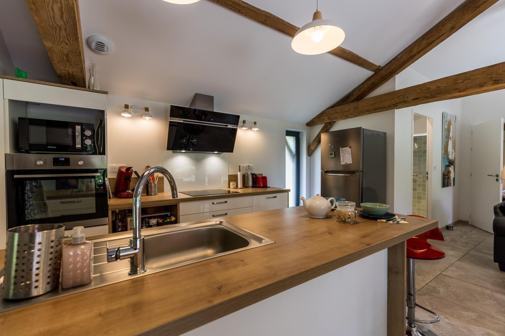 Une cuisine moderne dotée d’un plan de travail en bois, d’appareils électroménagers en acier inoxydable et d’un luminaire suspendu.
