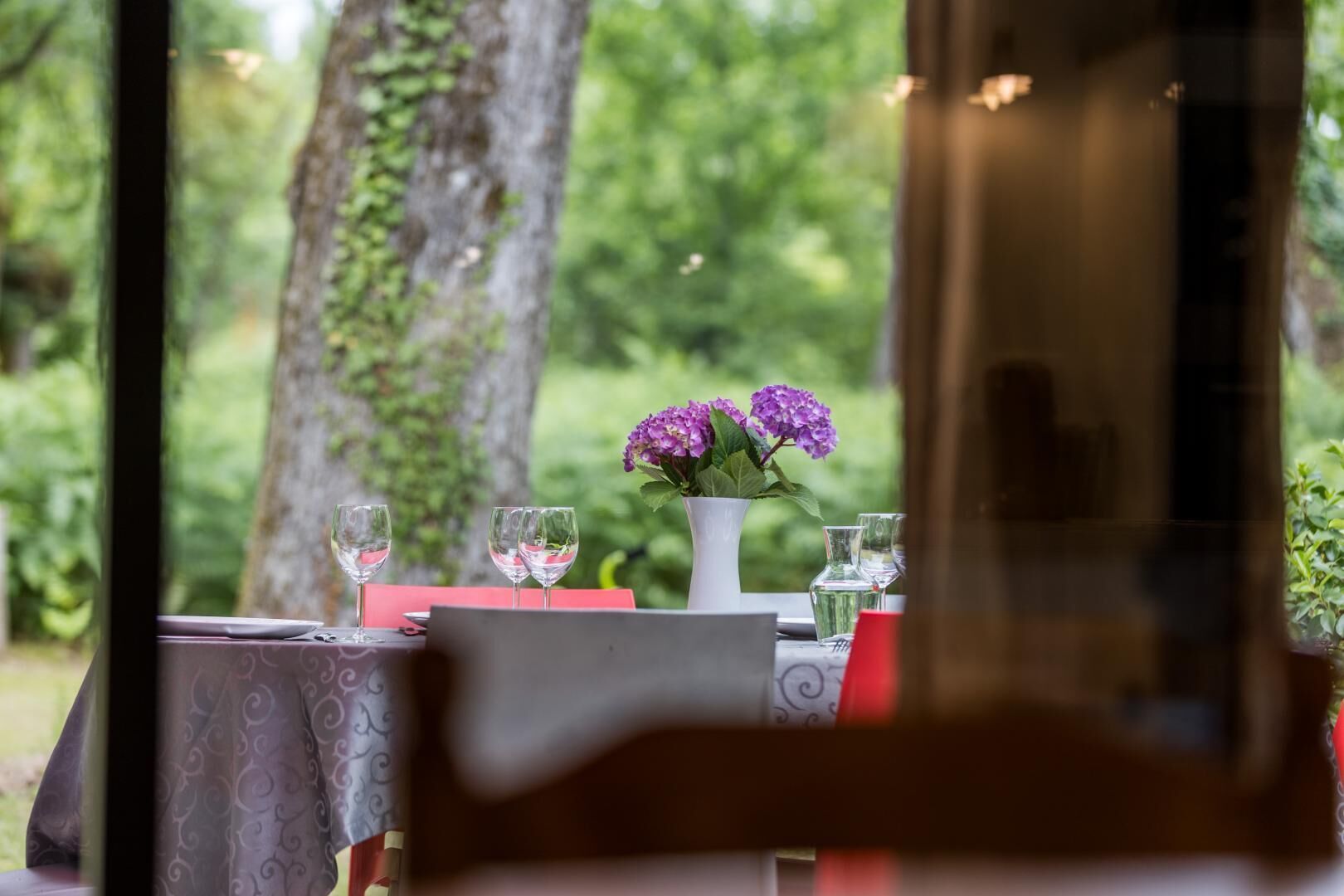 Une table avec un vase de fleurs violettes, des verres à vin et un ordinateur portable.