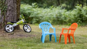 Deux chaises en plastique, une bleue et une orange, sont placées sur une pelouse. On aperçoit un arbre et un vélo vert en arrière-plan.