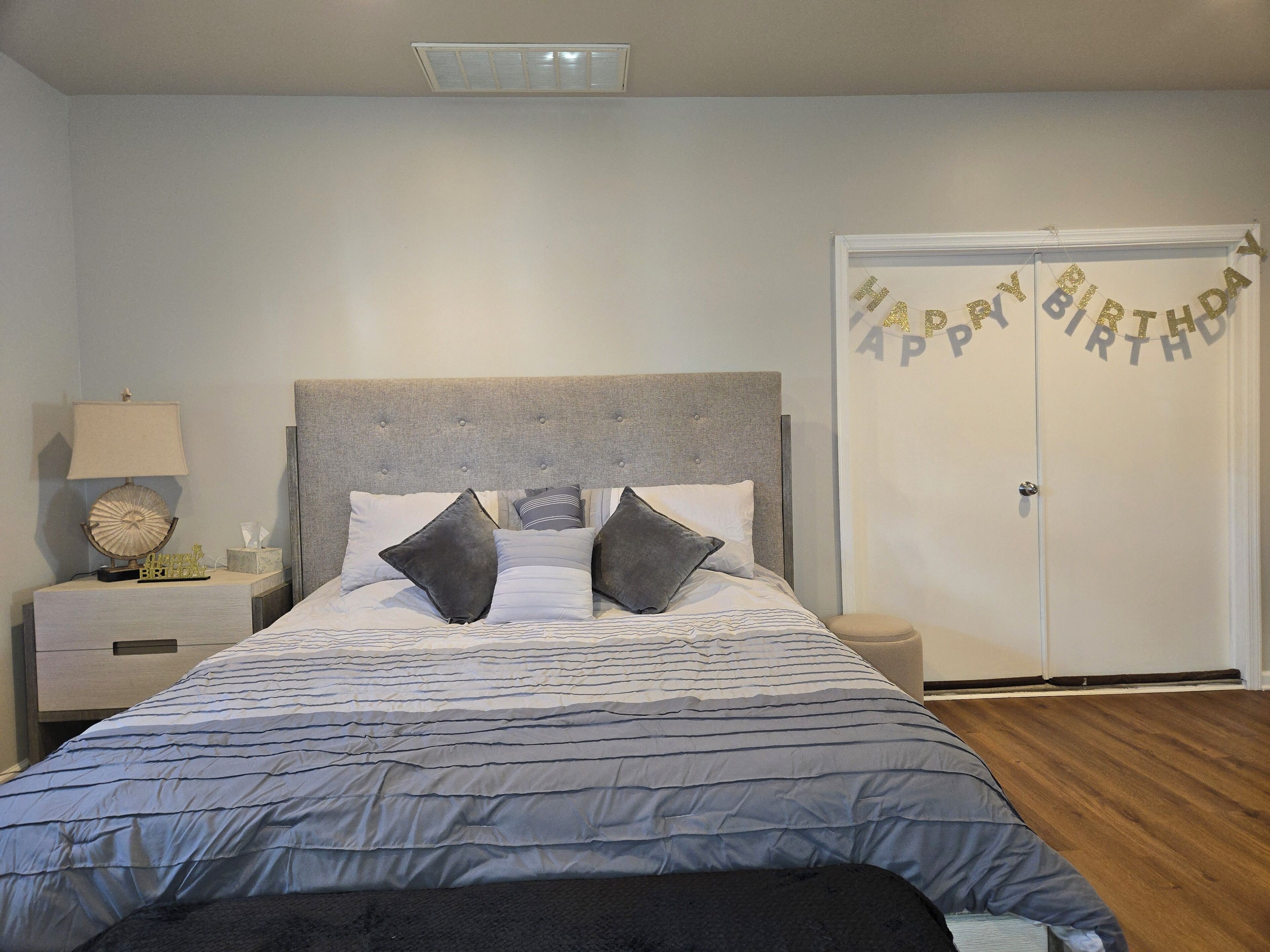 A bedroom with a bed, nightstands, a lamp, and a door with a birthday banner.