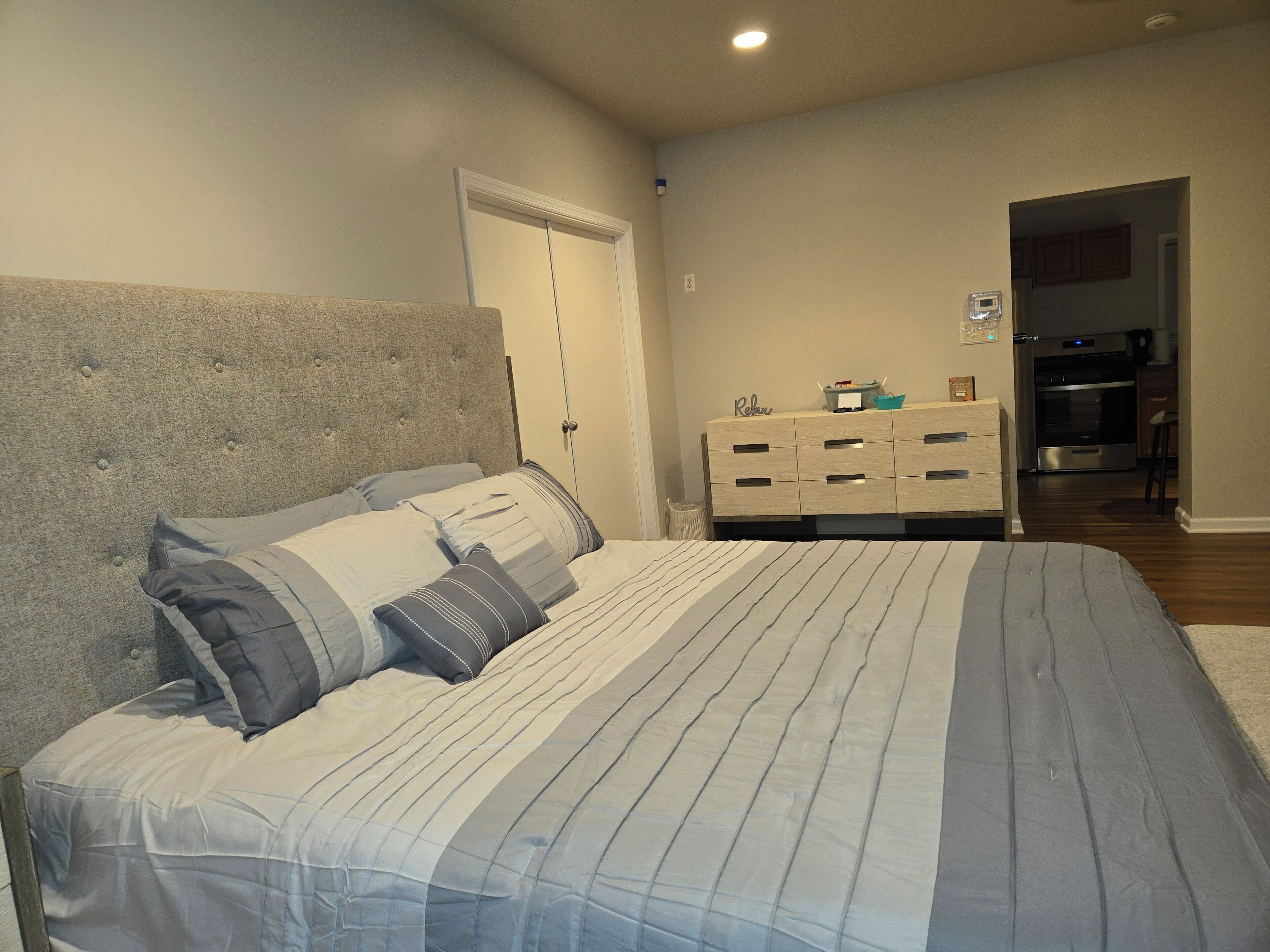 Ein Schlafzimmer mit einem Bett, einer Kommode und einer Tür zur Küche.