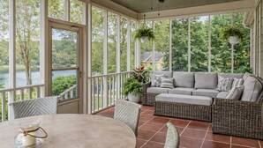 A covered patio with a wicker sofa, a round table, and hanging plants.