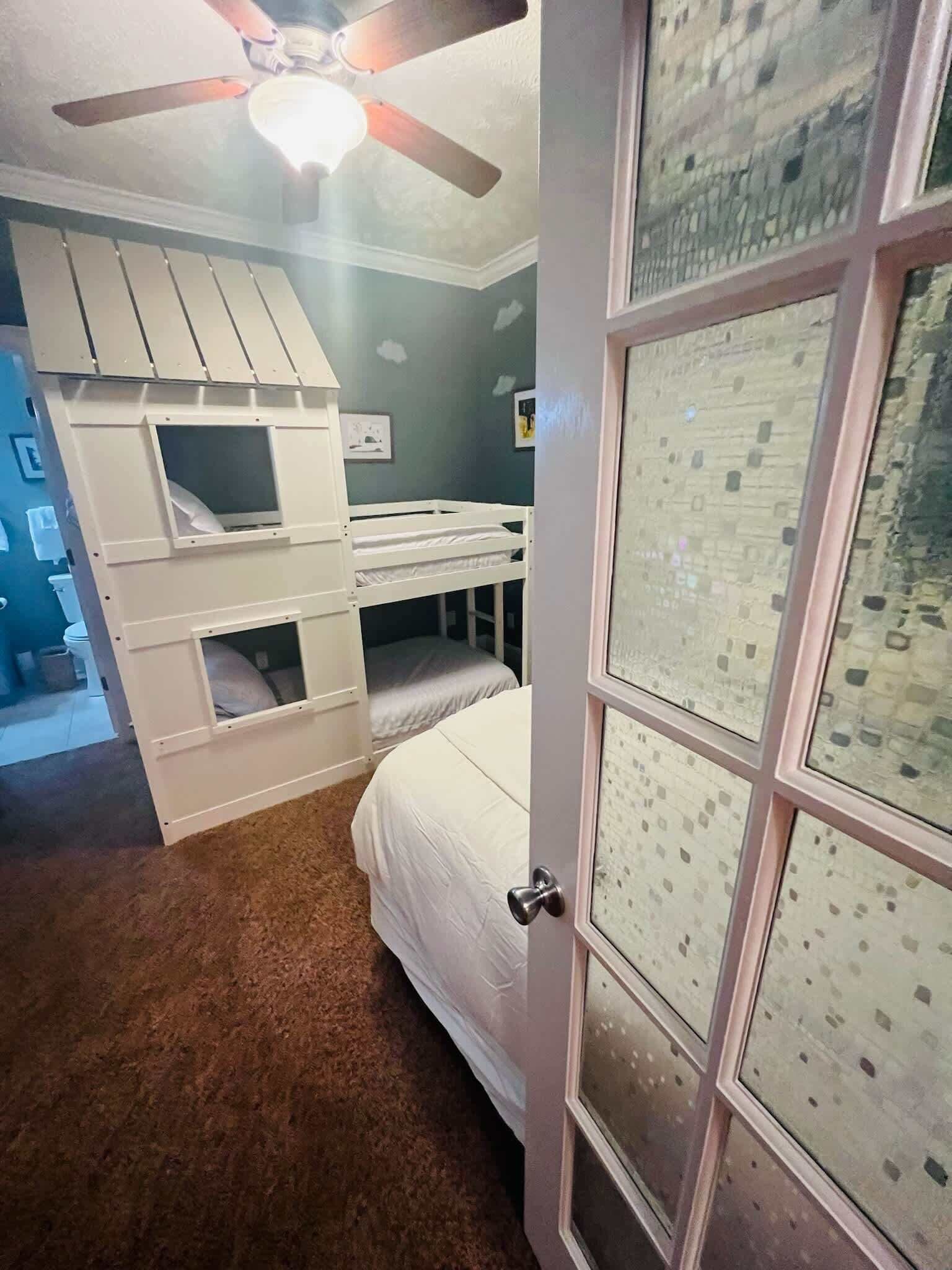 A bedroom with bunk beds, a ceiling fan, and a door with frosted glass panels.