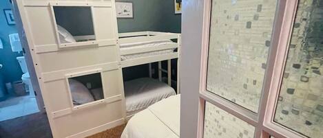 A bedroom with bunk beds, a ceiling fan, and a door with frosted glass panels.