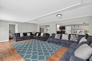 A modern living room with grey sofas, a patterned rug, and a kitchen in the background. - 4BR Spacious Paradise (Siesta Key)