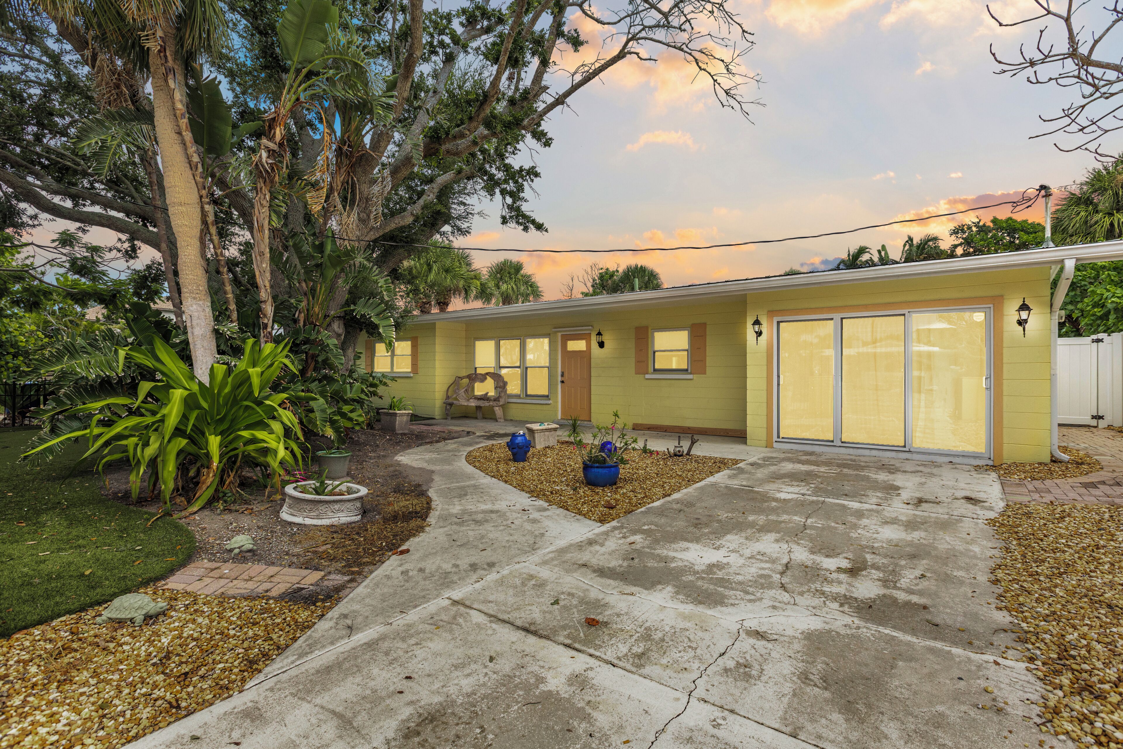 A single-story house with a front porch, a small garden with potted plants, and a concrete driveway.