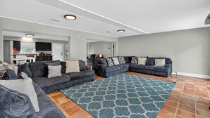 A spacious living room with a large sectional sofa, a patterned rug, and a kitchen in the background.