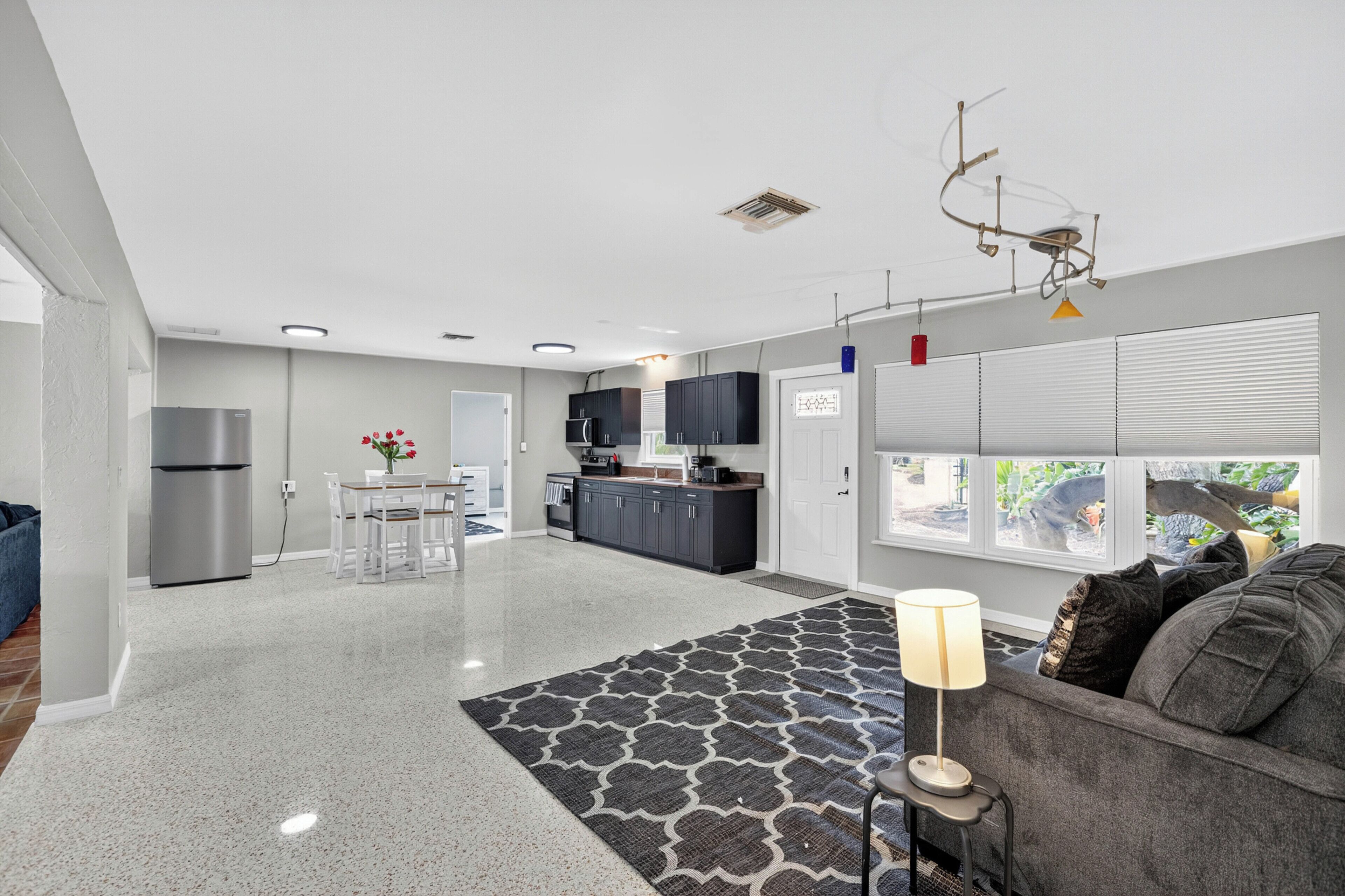 A modern kitchen with dark cabinets, a refrigerator, and a dining area with a table and chairs.