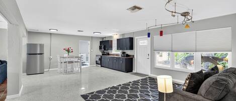 A modern kitchen with dark cabinets, a refrigerator, and a dining area with a table and chairs.