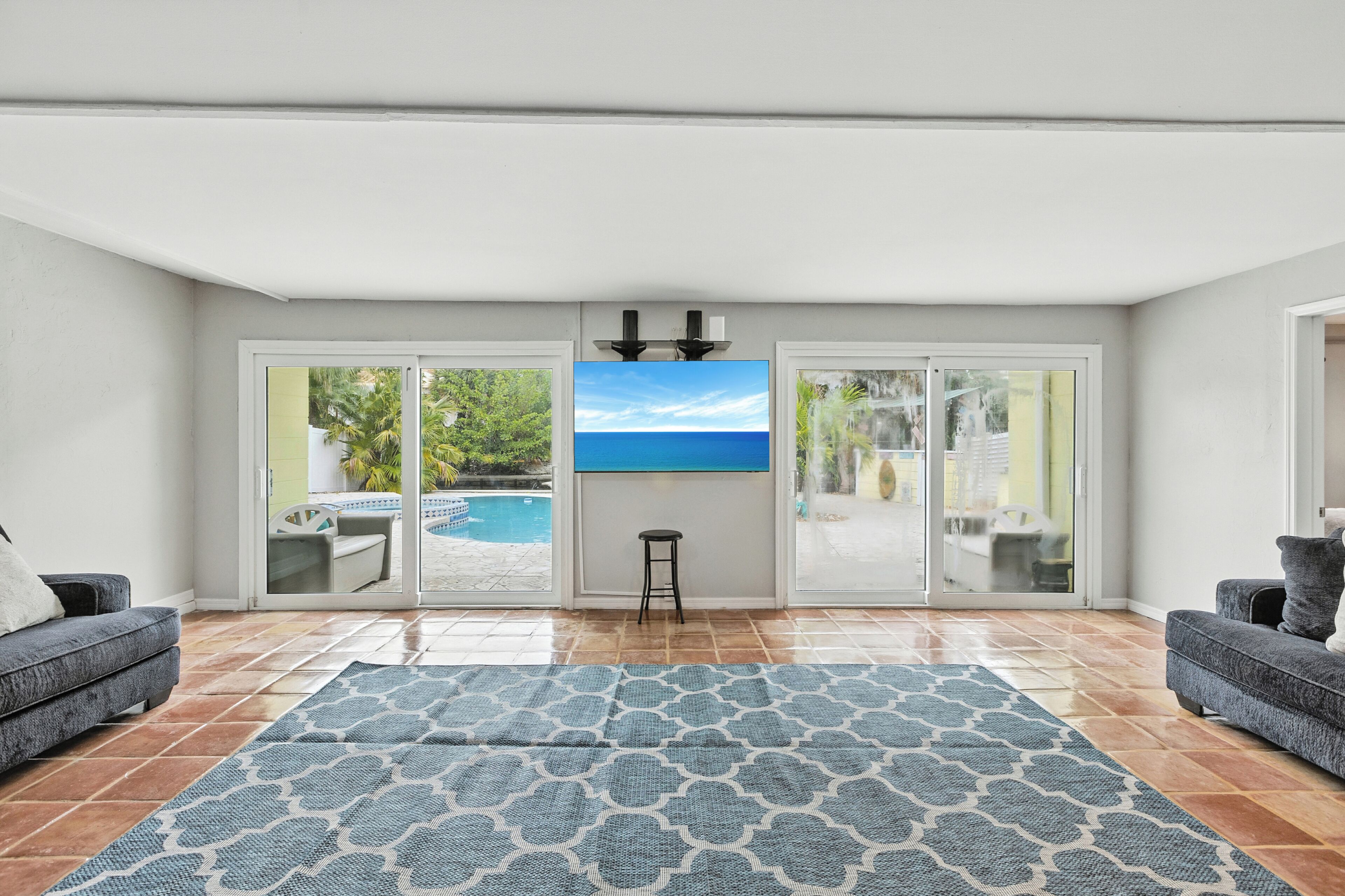 A living room with a large window, a pool view, and a blue patterned rug.