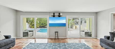 A living room with a large window, a pool view, and a blue patterned rug.