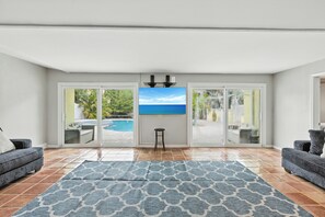 A living room with a large window, a pool view, and a blue patterned rug. - 4BR Spacious Paradise (Siesta Key)