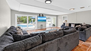 A modern living room with a sectional sofa, a flat-screen TV, and a view of a pool through glass doors.