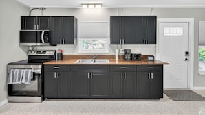 A modern kitchen with dark cabinets, stainless steel appliances, a granite countertop, and a window with blinds.