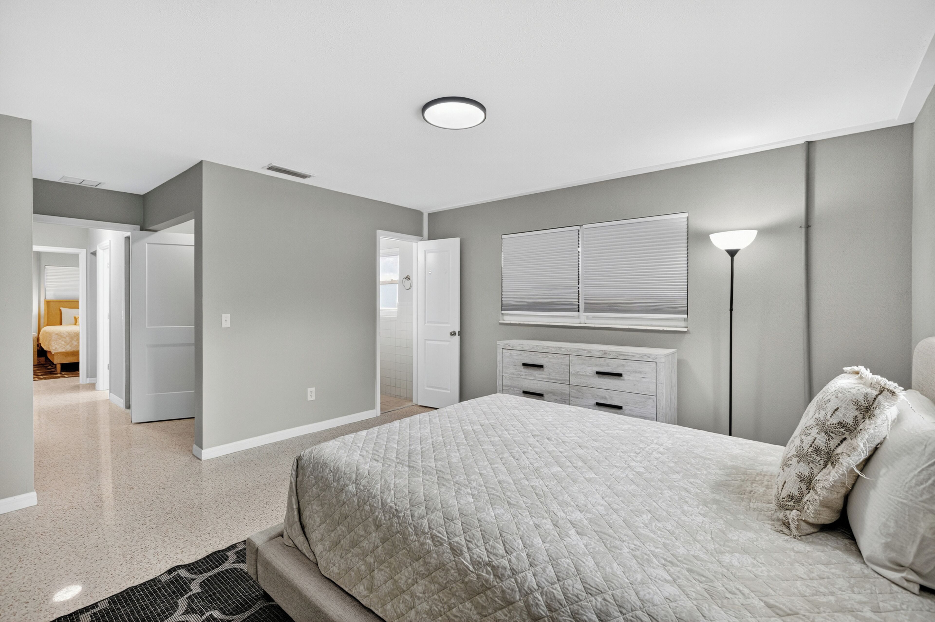 A bedroom with a bed, a dresser, a nightstand, a lamp, and a door leading to another room.