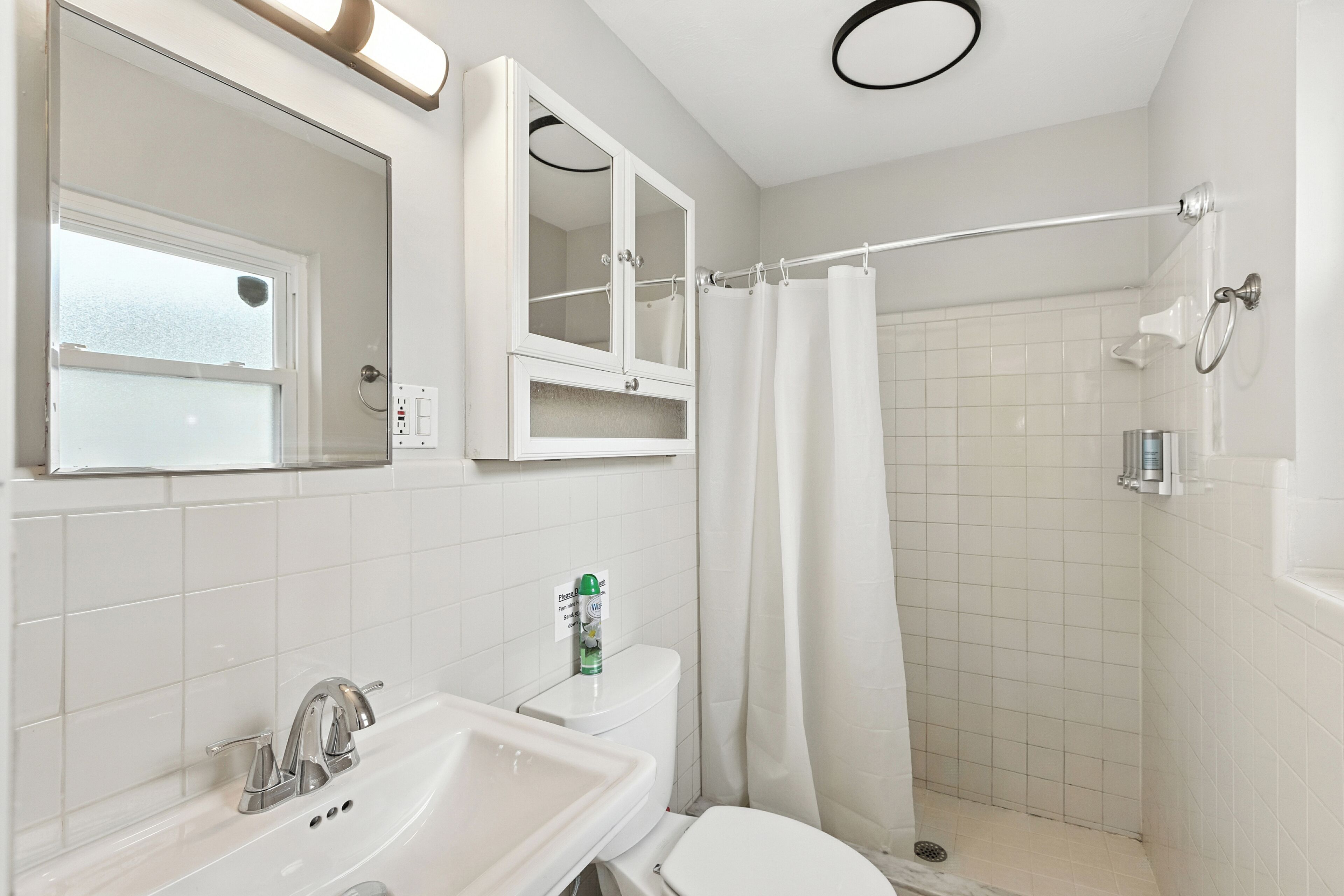 A bathroom with a sink, mirror, toilet, and shower area.
