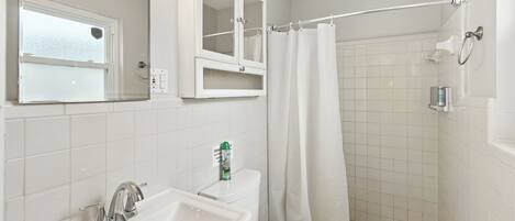 A bathroom with a sink, mirror, toilet, and shower area.