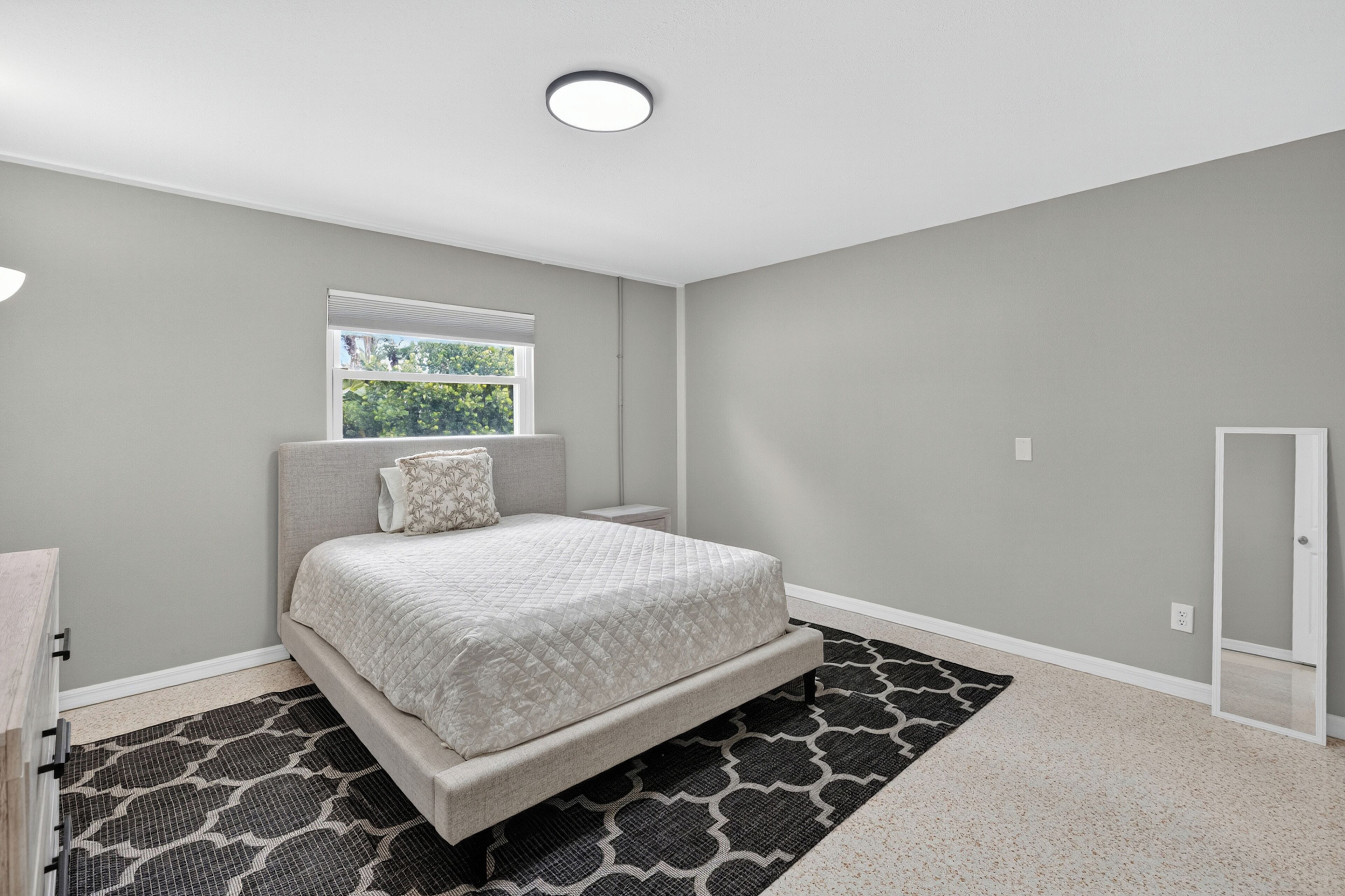 A bedroom with a bed, a window, a door, and a ceiling light.