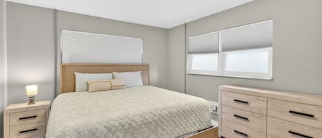 Un dormitorio con cama, mesitas de noche, cómoda, ventana con persianas e iluminación en el techo.
