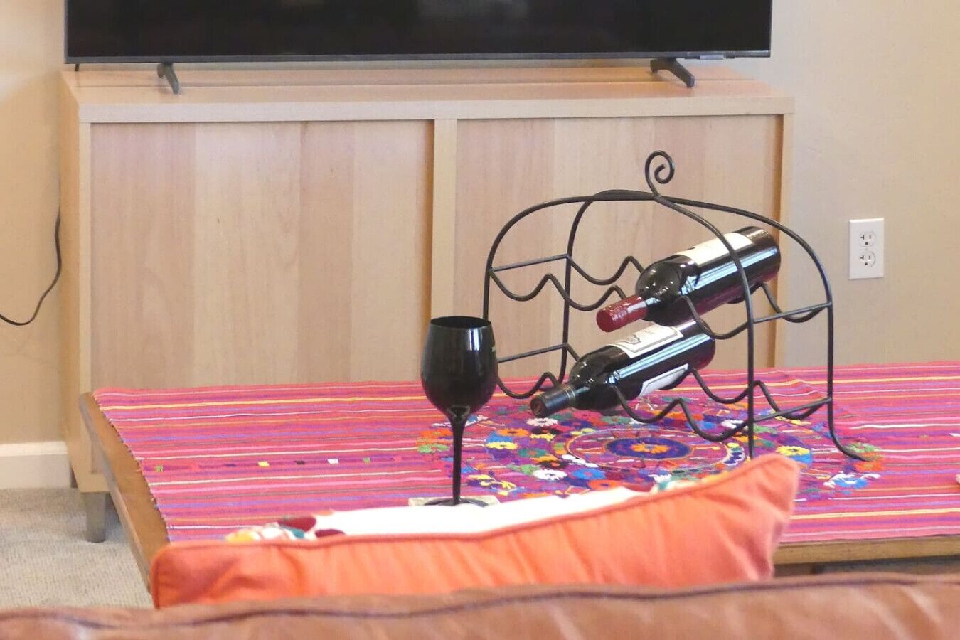 A bed with a colorful bedspread, a wine glass, and a wine bottle on a metal stand.