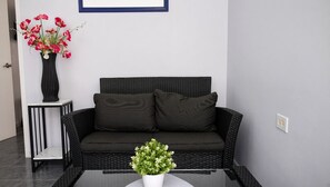 A black wicker sofa with two cushions, a small white table with a vase of flowers, and a potted plant on a glass table. - Sunway Aruba Aparments (Santa Cruz)