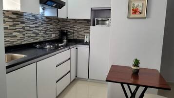 Eine moderne Küche mit weißen Schränken, einer schwarzen Arbeitsplatte, einem eingebauten Backofen und einem kleinen Tisch mit einem Topfplanzen.