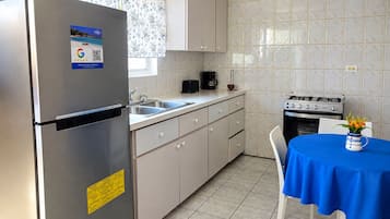 Cozinha compacta com geladeira de aço inoxidável, cafeteira, fogão e mesa com toalha de mesa azul.