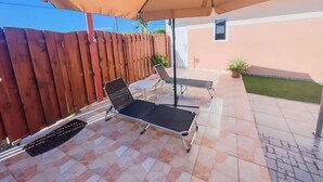 An outdoor patio with two lounge chairs under a large umbrella, a small table, and a potted plant. - Sunway Aruba Aparments (Santa Cruz)