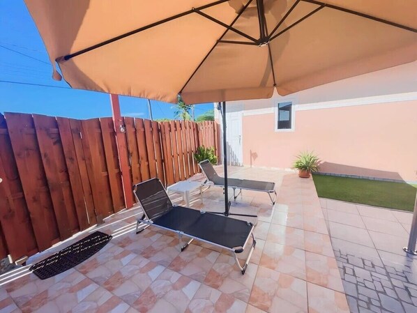 An outdoor patio with two lounge chairs under a large umbrella, a small table, and a potted plant. - Sunway Aruba Aparments (Santa Cruz)