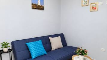 Um sofá azul com duas almofadas, uma mesinha redonda com uma planta em vaso e um quadro na parede.