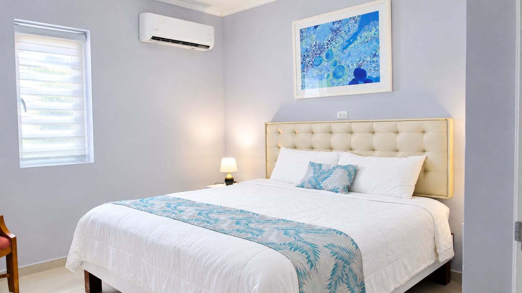 A bedroom with a bed, a nightstand, a lamp, an air conditioning unit, and a window.
