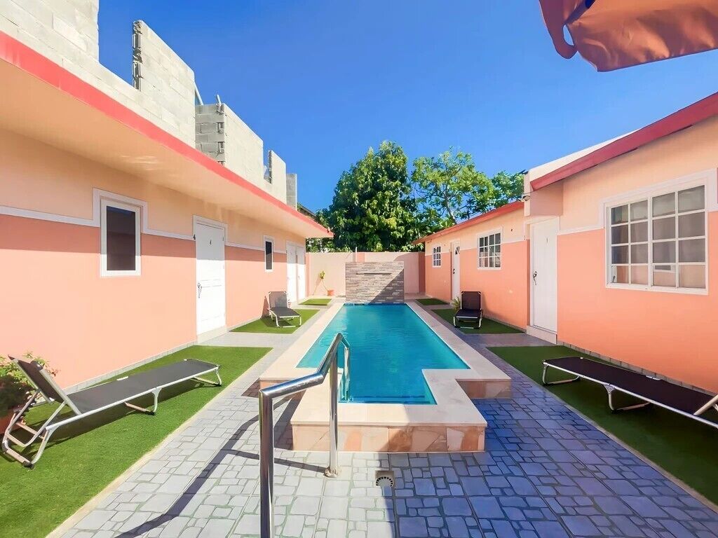 Una piscina con borde de piedra, rodeada de sillas de descanso y un camino empedrado.