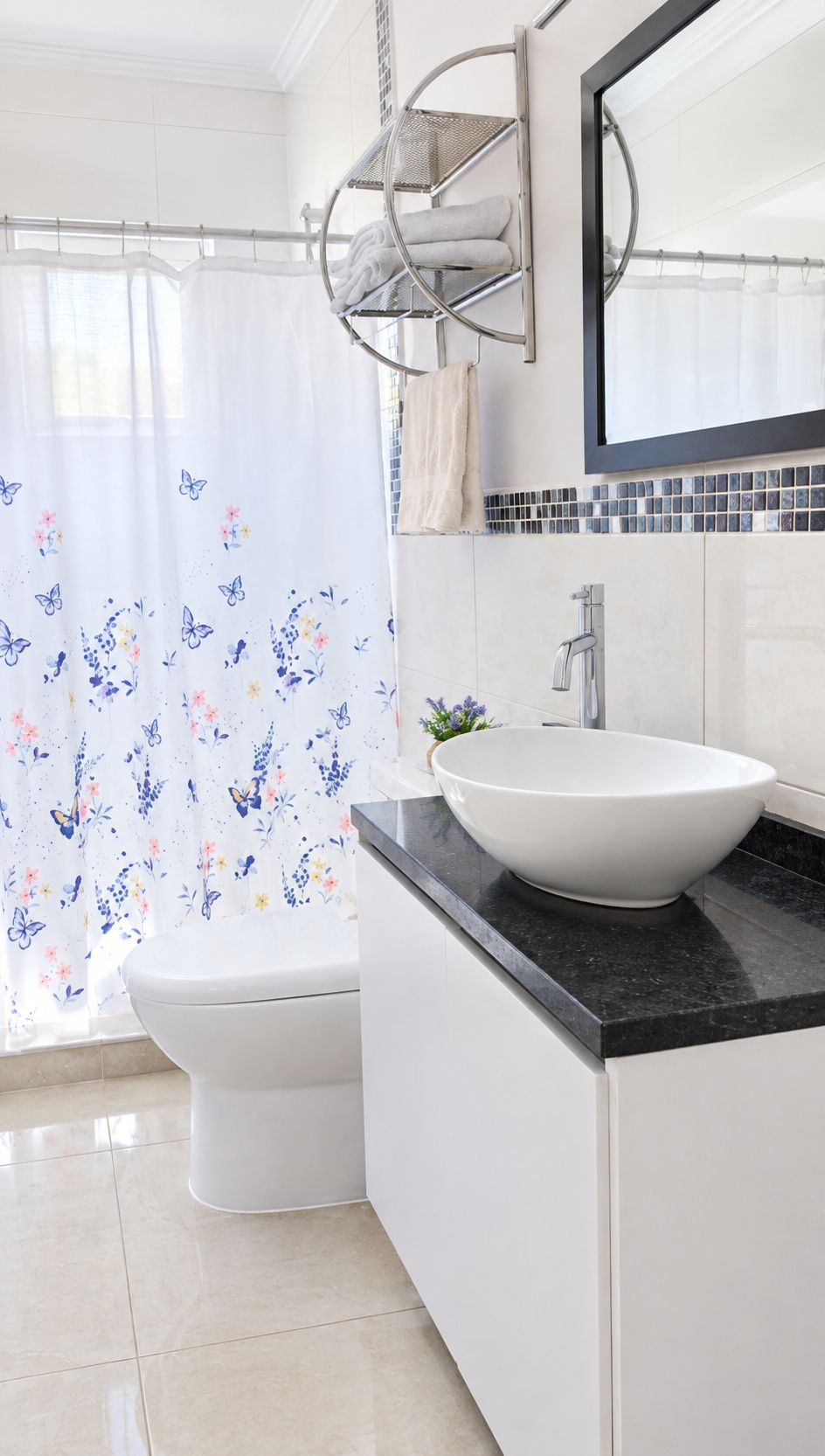 Ein Badezimmer mit einer weißen Toilette, einem weißen Waschbecken mit schwarzer Arbeitsplatte, einem Handtuchhalter und einem Duschvorhang mit Blumenmuster.
