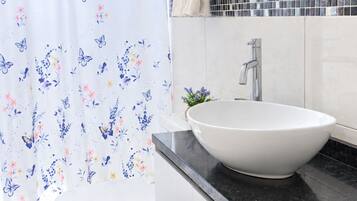Ein Badezimmer mit einer weißen Toilette, einem weißen Waschbecken mit schwarzer Arbeitsplatte, einem Handtuchhalter und einem Duschvorhang mit Blumenmuster.