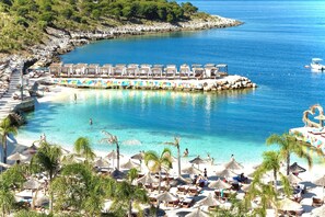 Un complejo turístico en la playa con tumbonas, sombrillas y una piscina.