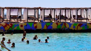 A pool area with people swimming and lounging under shaded structures. - Mucobega Hotel  (Sarande)