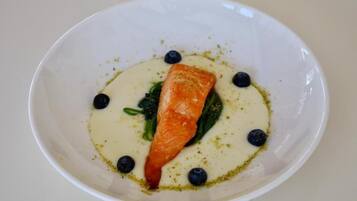 Un tazón blanco con un filete de salmón, arándanos y salsa cremosa.